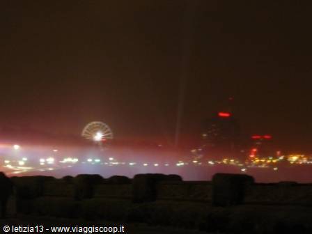 Foggy night on the waterfront: illuminated ferris wheel and red-lit skyscrapers behind