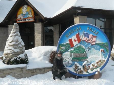 Tourist in winter jacket next to the snowy Niagara Falls sign