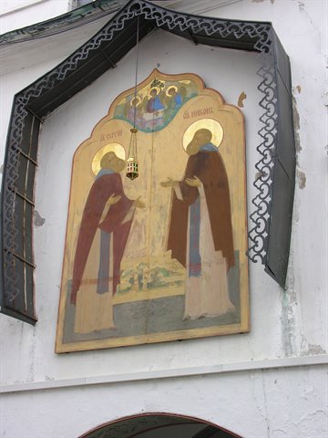 Fresco of two saints under a wrought-iron canopy on a white wall
