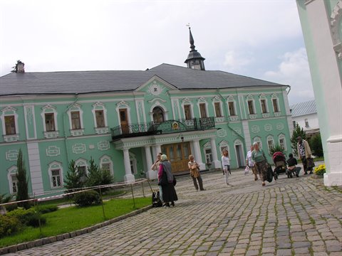 Tourists walk on cobblestones in front of a pale green building with grey roof