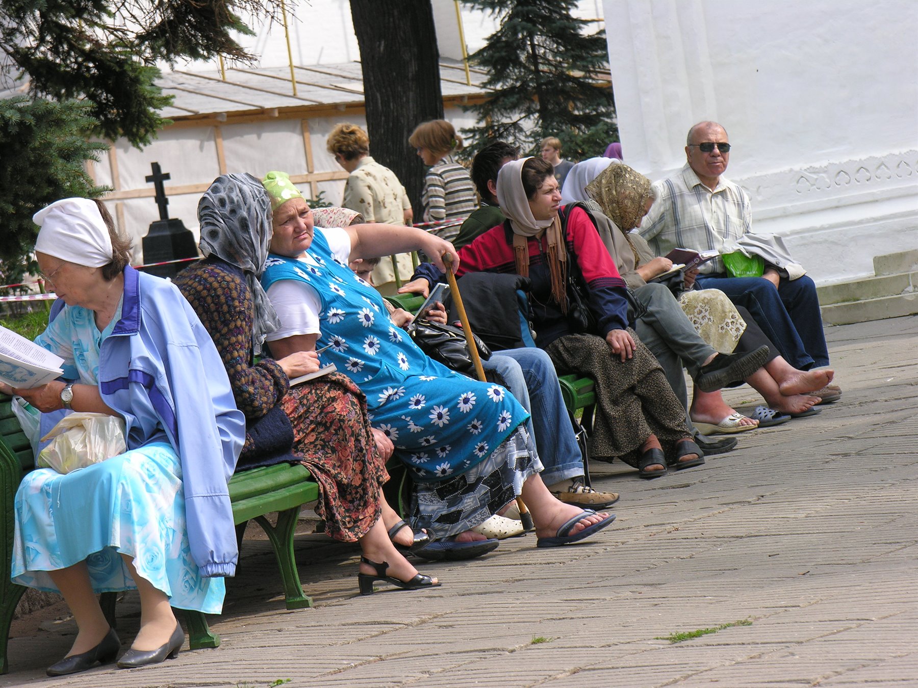 Donne anziane con foulard sedute su panchine verdi in cortile di monastero