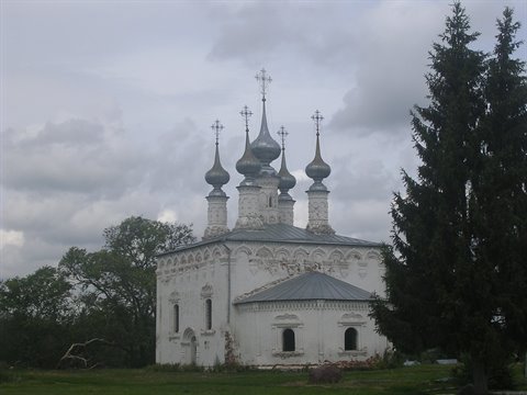 White church with silver onion domes beside fir trees, cloudy sky