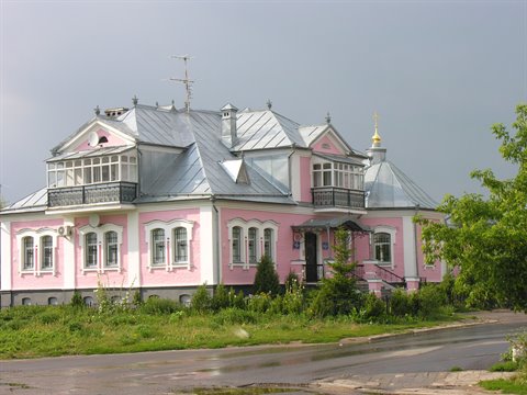 Pink wooden mansion with silvery metal roof, white verandas, overcast gray sky