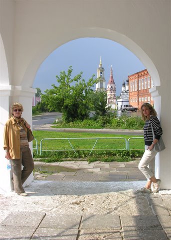 Two women under a white archway, church towers and brick walls behind