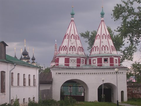 White monastery gate with two red tent-roofed towers under a grey sky