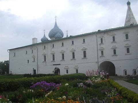 White walls of Rostov Kremlin with blue onion domes under cloudy sky