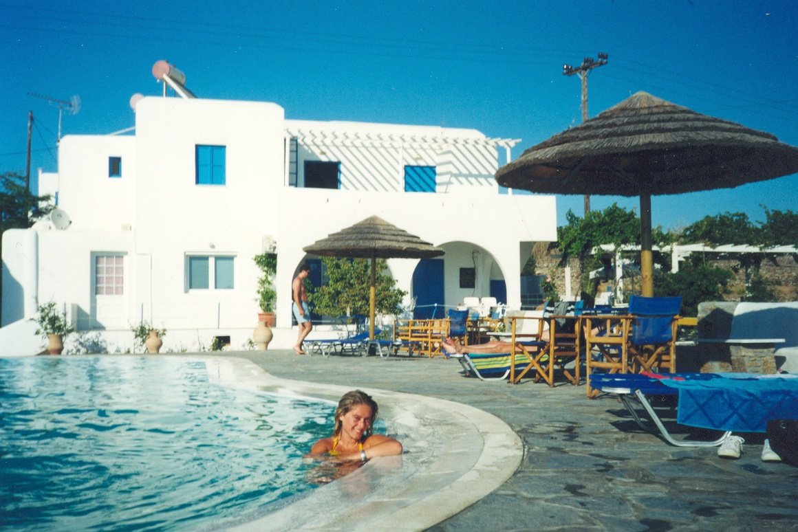 Turista nuota in piscina accanto a hotel bianco con ombrelloni di paglia