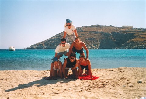 Six friends form a human pyramid on the sand by turquoise sea