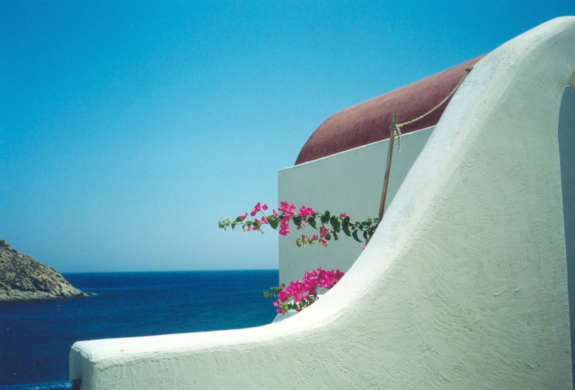 Muro bianco curvo con bouganville rosa sopra il mare blu, cielo sereno