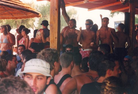 Beach bar party, shirtless young people dancing under wooden beams