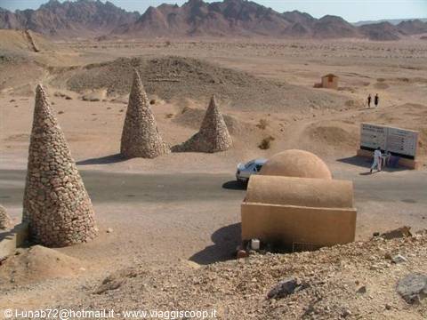 Stone cone piles and mud-brick dome in the desert, people by a sign