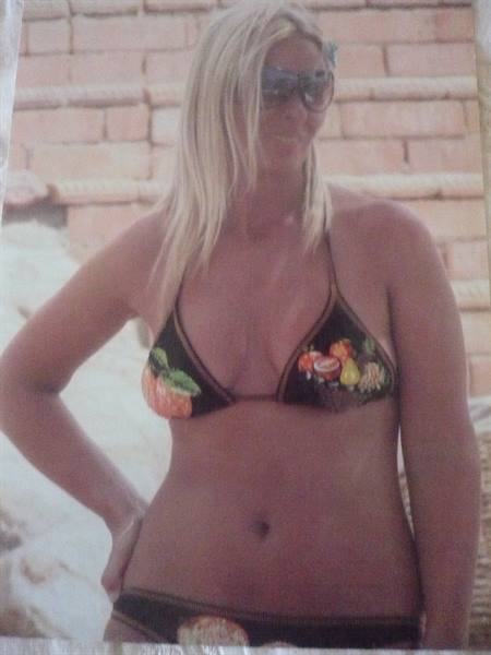 Blonde woman in sunglasses and black printed bikini near a brick wall