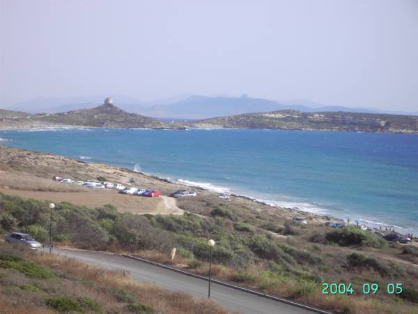 Parked cars along turquoise sea coast, old stone tower on rocky headland
