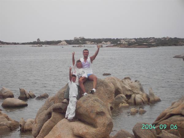 Woman and two children waving atop granite rocks by calm water