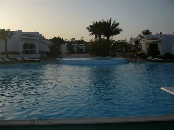 Resort pool at dusk, palm trees, white sun loungers and whitewashed bungalows