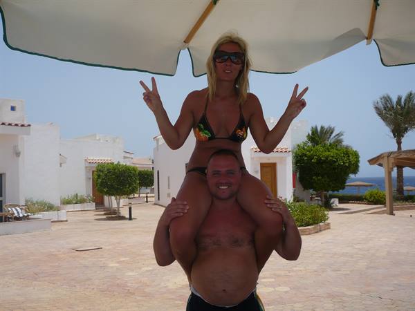 Woman in bikini gives peace signs on man's shoulders under beach umbrella