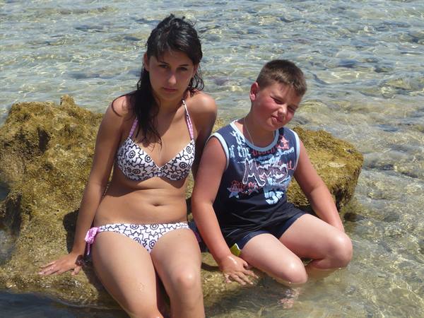 Two kids sitting on a rock in shallow clear sea water