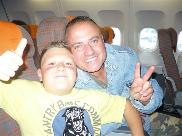 Smiling father and son on plaid airplane seats, thumbs up and peace sign