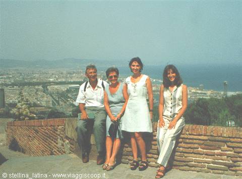 Four people pose on a brick wall, city and sea in the background