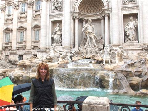Woman in front of Trevi Fountain with marble statues and umbrellas