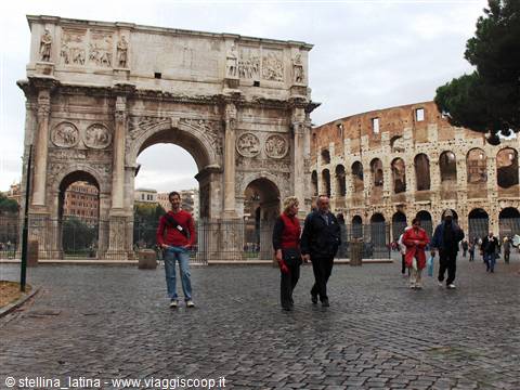 Tourists walk on cobblestones in front of the Arch of Constantine and the Colosseum