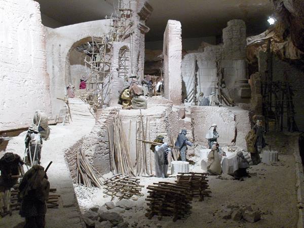 Nativity scene with figurines among tufa ruins, wooden scaffolding under artificial light