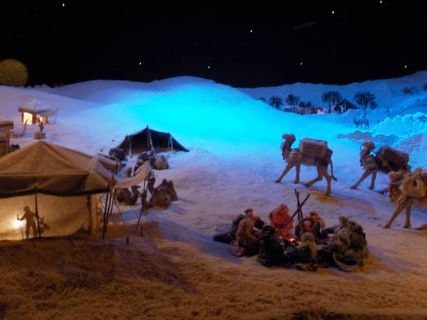 Night diorama: loaded camels and figures gathered around fire beside tents
