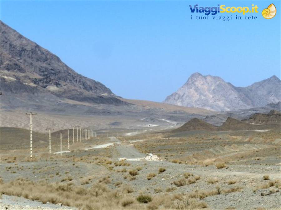 Dirt road crossing arid mountains, power line poles, blue sky, desert area