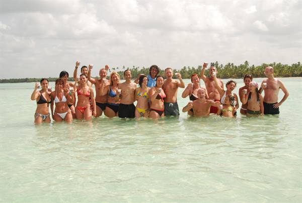 Group of tourists in swimwear toasting in shallow turquoise water by the beach