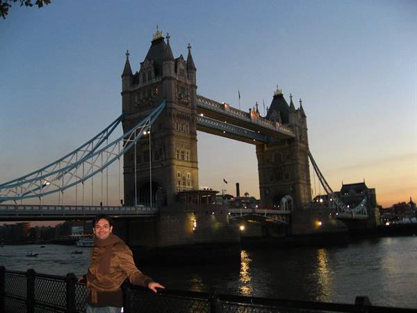 Man by the railing in front of illuminated Tower Bridge at dusk