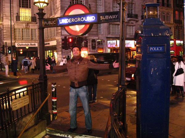 Tourist with open arms under the Underground sign at Piccadilly Circus, evening