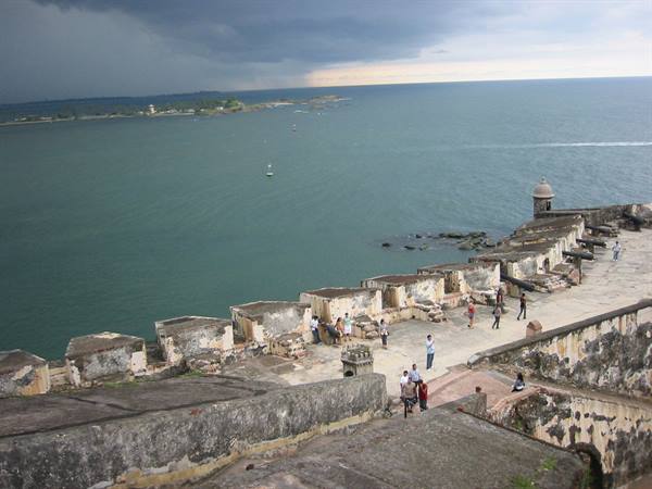 Tourists on stone ramparts of Castillo San Felipe del Morro facing cloudy sea