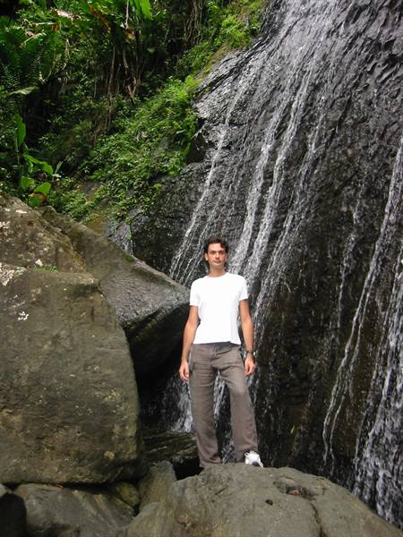 Man in white t-shirt standing on rocks in front of a waterfall