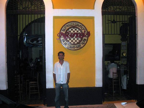 Man in white shirt outside Nanny's bar, yellow facade with arches