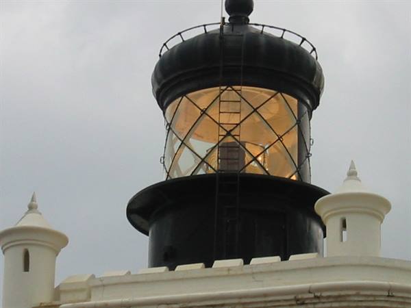 Black lighthouse lantern with lit glass and metal ladder, gray sky