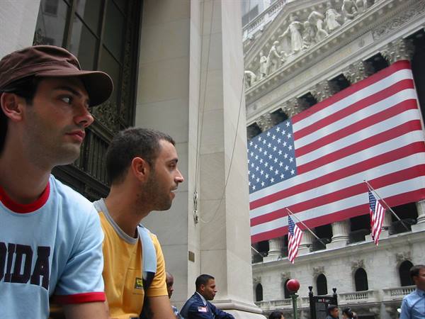 Two young men in front of the New York Stock Exchange with American flag, Wall Street
