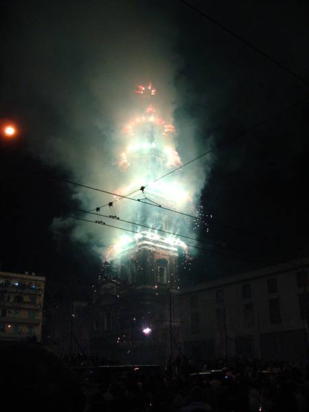 Fireworks light up a bell tower over a crowded square at night