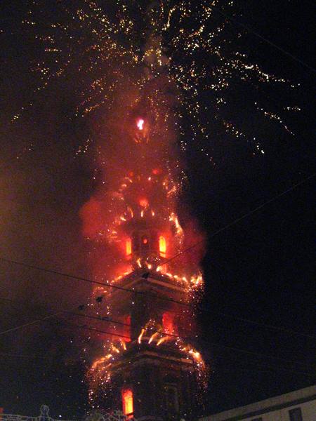 Tower wrapped in red and golden fireworks against the night sky