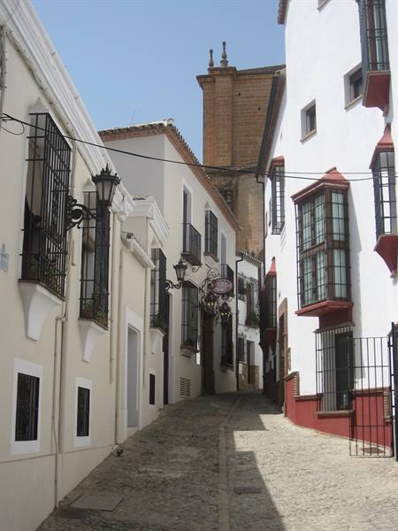 Cobbled alley between whitewashed houses with iron balconies, stone church behind