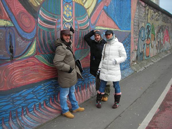 Three tourists in coats in front of the painted murals at East Side Gallery, Berlin