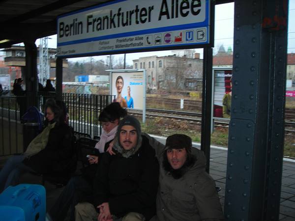 Travelers sitting on the platform of Berlin Frankfurter Allee station, gray daylight