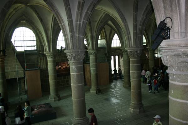 Inside Mont-Saint-Michel abbey, gothic columns and vaults, visitors walking