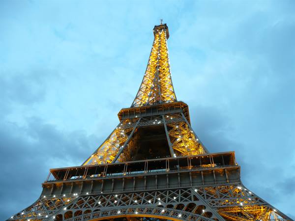 Eiffel Tower glowing with golden lights against a cloudy evening sky