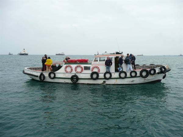 Old white boat with spare tires on the side, passengers at open sea