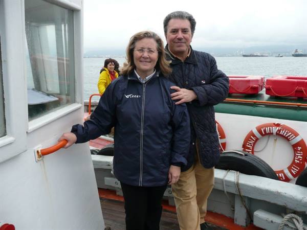 Couple in windbreakers on a ferry deck, red lifebuoys, gray sea