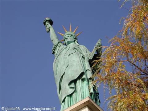 Green copper Statue of Liberty replica holding torch beside autumn branches