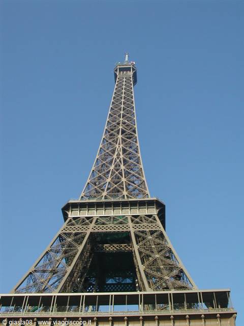 The Eiffel Tower's iron lattice rises against a clear blue sky