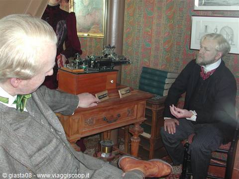 Wax figures in a Victorian room around an antique telephone device