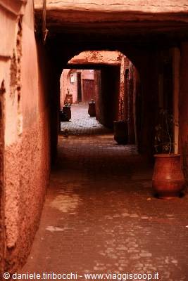 Red brick alleyway with arch and clay pots in the medina