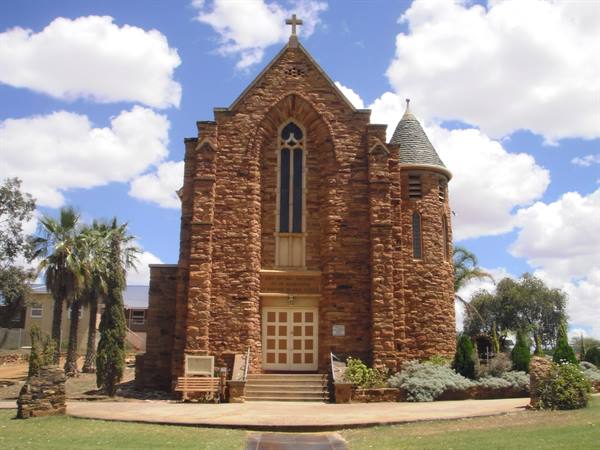 Red stone church with conical tower, palm trees and cloudy sky